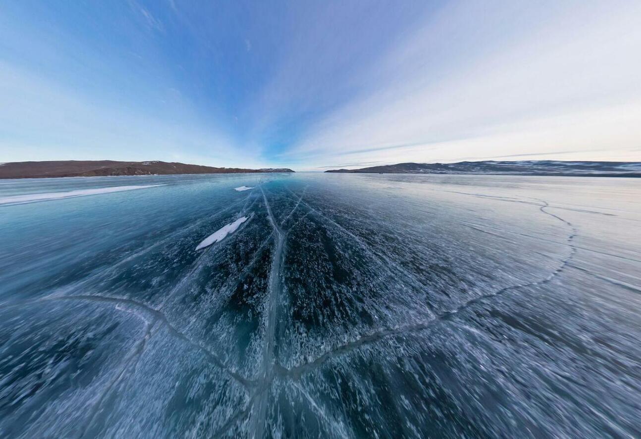 Blue transparent ice of Lake Baikal covered with deep cracks under cloudy weather in Siberia, Russia